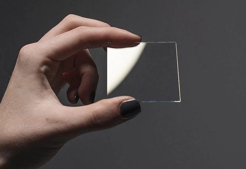 Researcher inspecting a transparent piezoelectric thin film specimen for electrical metrology characterization